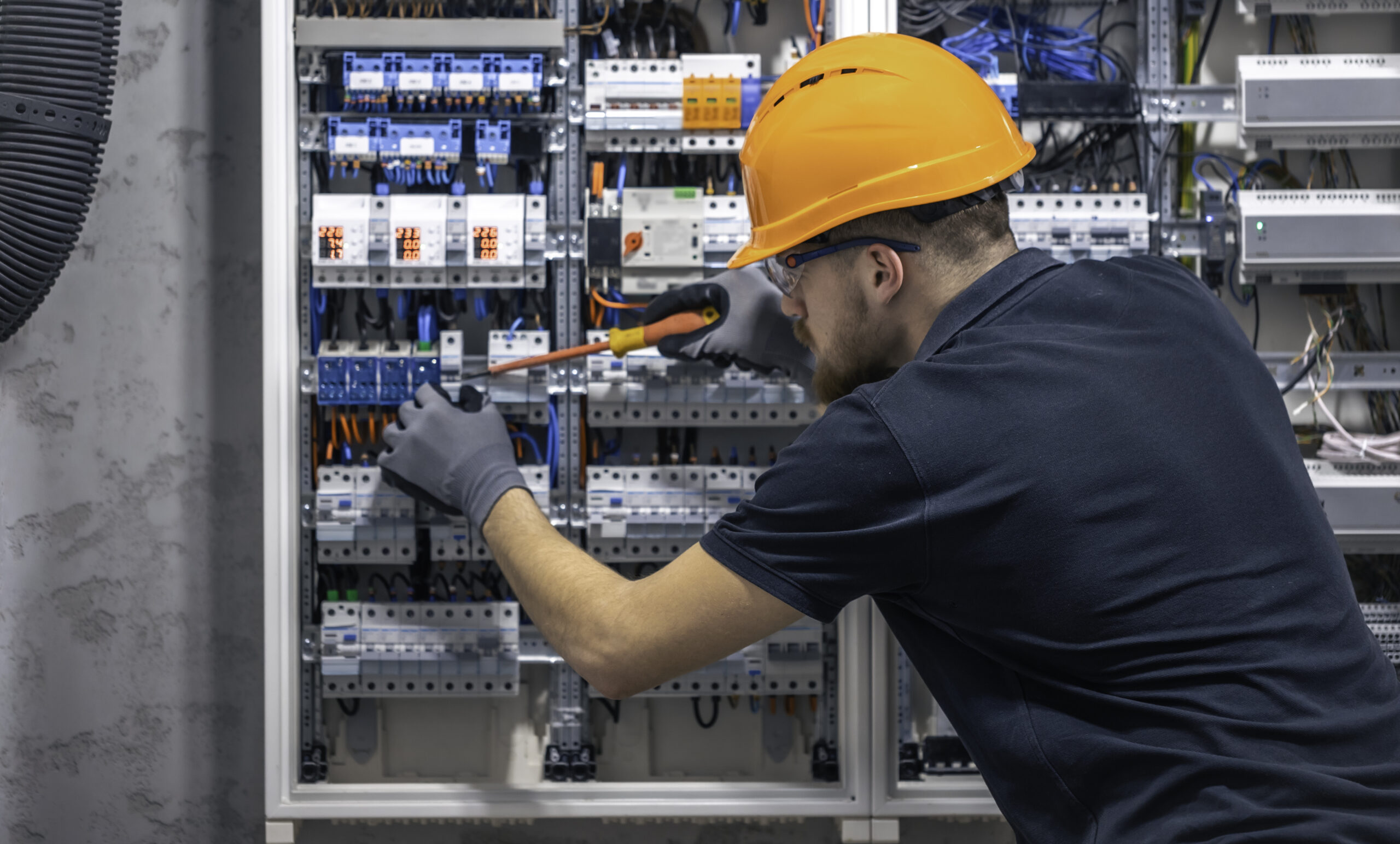 young adult electrician civil engineer screwing equipment into fuse box.