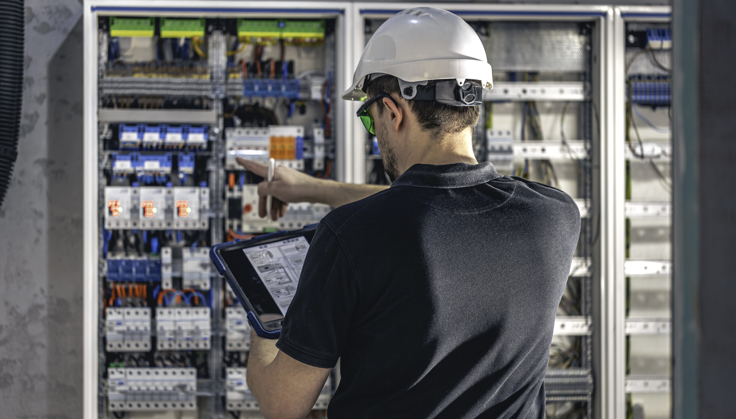 man, an electrical working in a switchboard with fuses, uses a tablet.